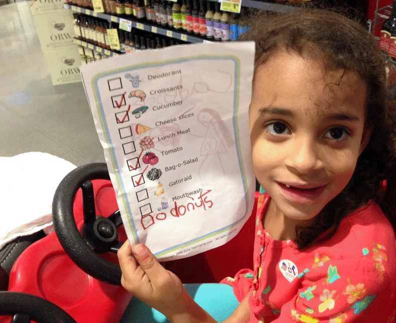 Girl in red grocery cart holding printed picture grocery list