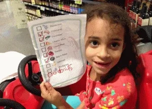 Girl in grocery cart kid car holding a picture grocery list with hand-written checkbox for DONUTS
