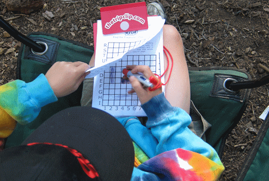 Child using paper battleship game with clipboard and attached pen while camping.